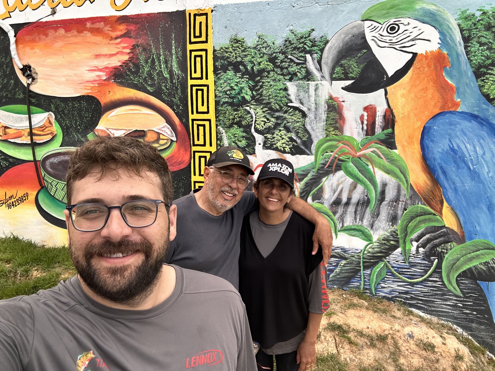 Tiago with his parents in front of a Brazilian parrot mural